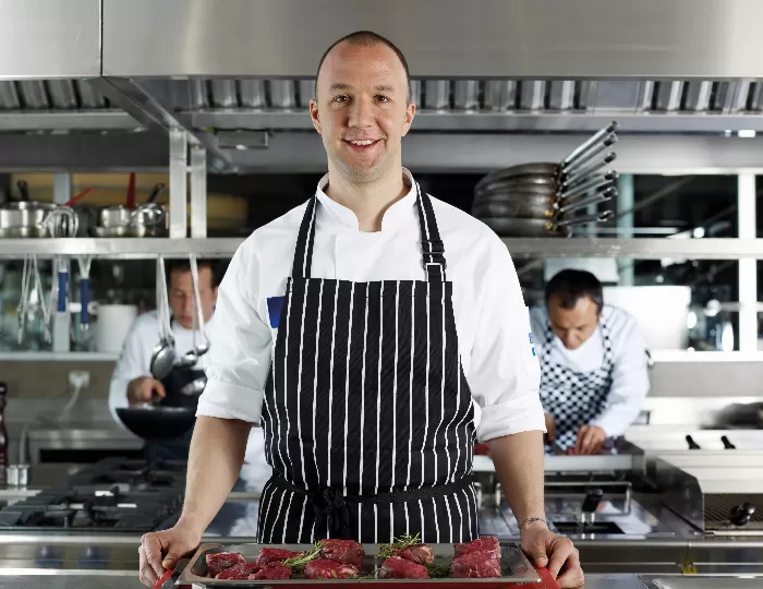 A chef in a stripy apron standing in a professional kitchen