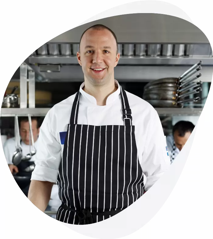 A chef in a stripy apron standing in a professional kitchen