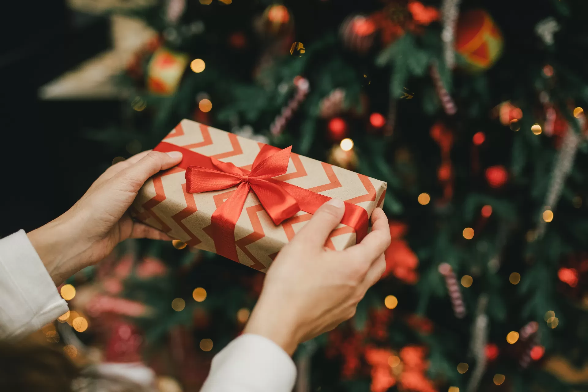 A wrapped gift with an orange bow in front of a Christmas tree