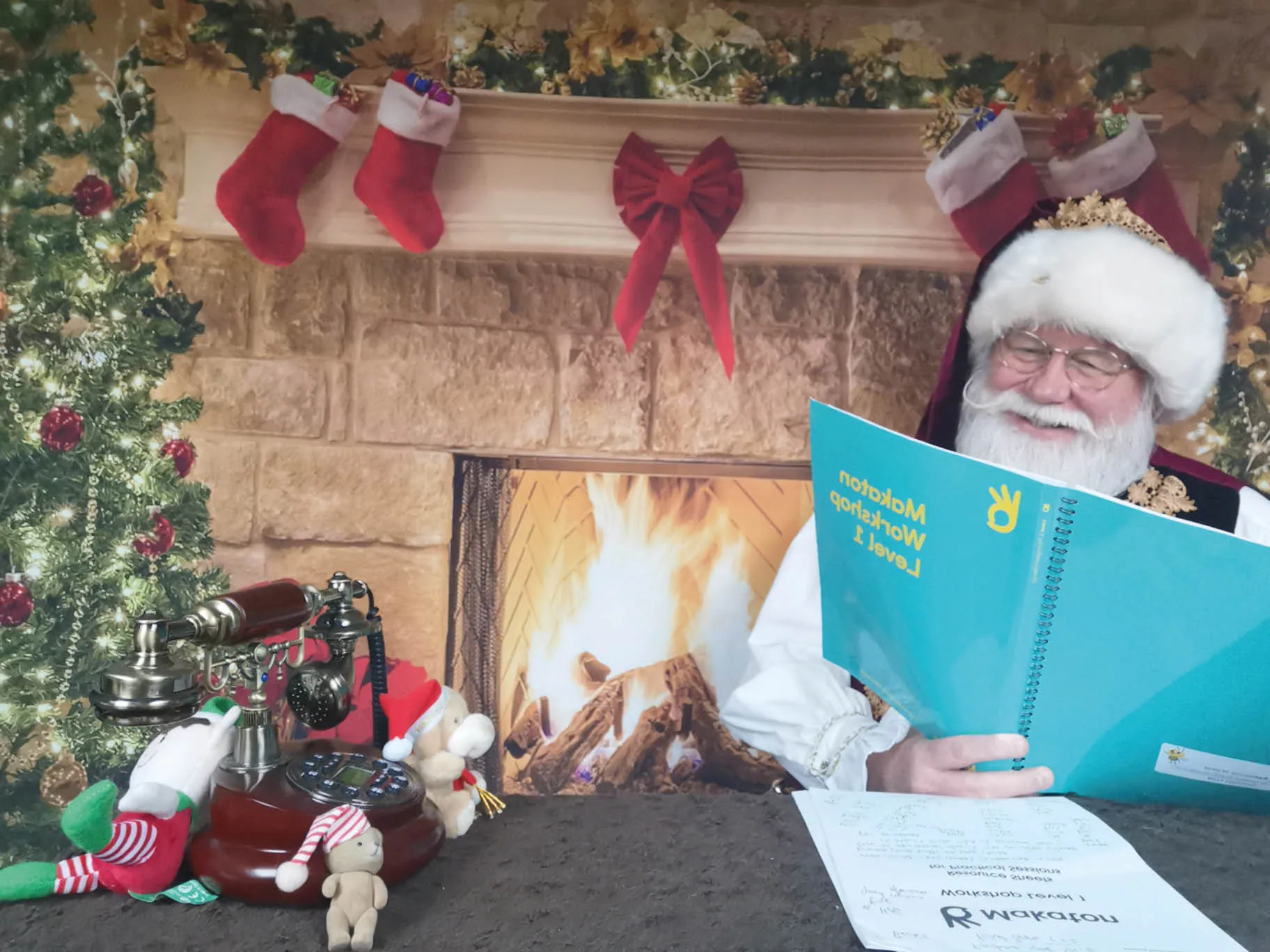 Santa reading a book sat by the fireplace.