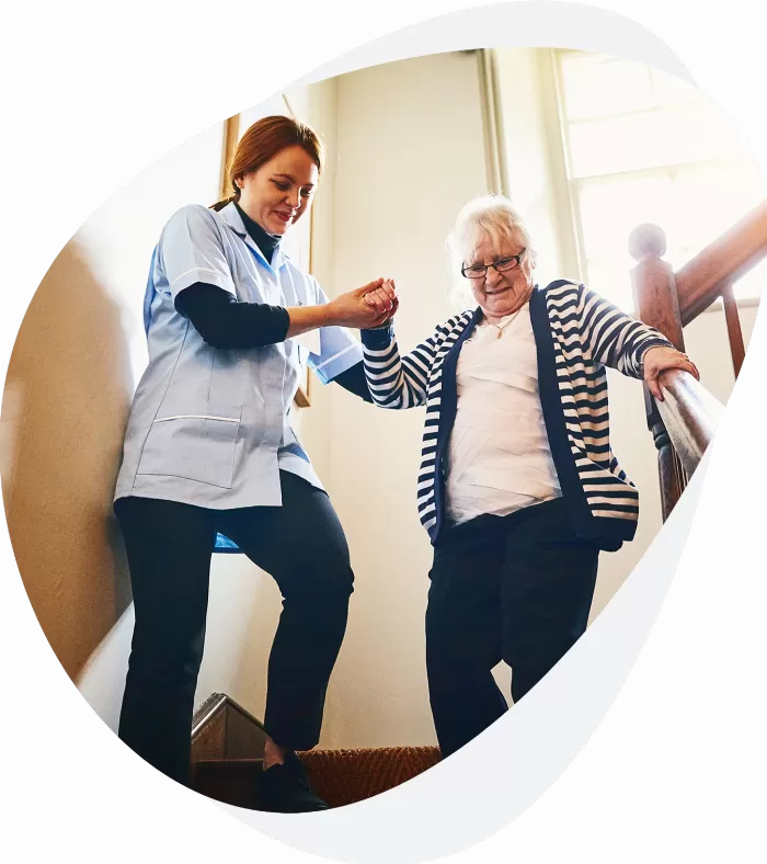 A woman helping an elderly lady down the stairs on a Busy Bees Education and Training adult health and social care apprenticeship.