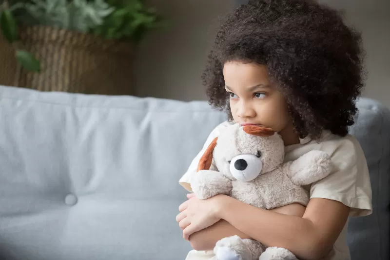 A curly haired child hugging a bear