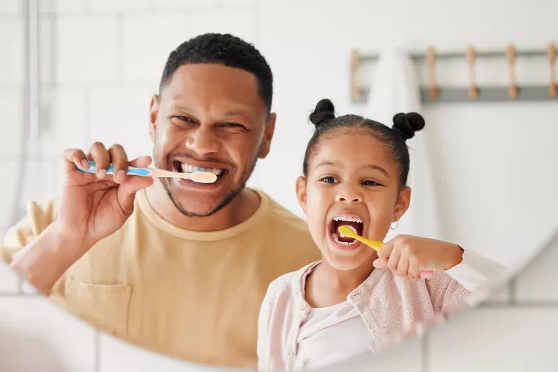 A young girl brushing her teeth with dad